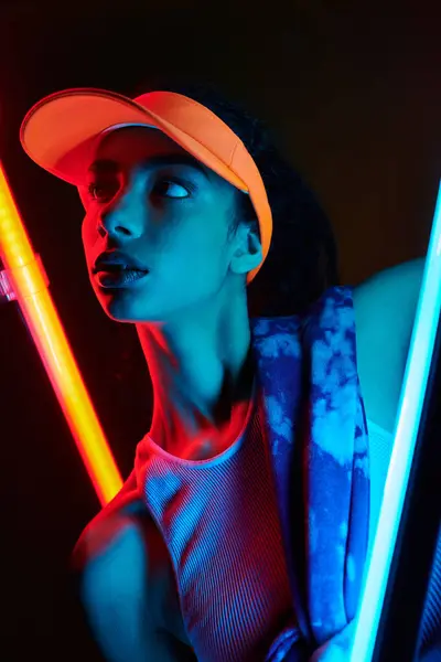 A young woman with vibrant orange hair in a bright orange visor poses against a backdrop of red and blue neon lights. — Stock Photo