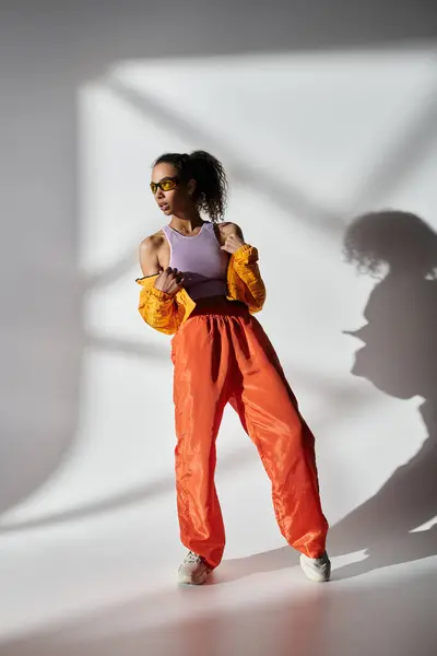 A stylish woman in a yellow jacket and orange pants poses against a grey backdrop, creating a bold and vibrant look. — Stock Photo