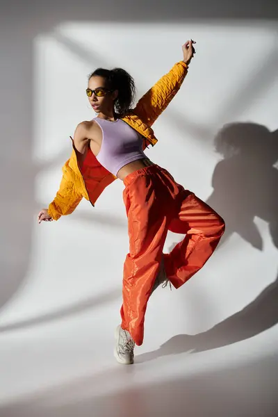 Una giovane donna afroamericana posa in uno studio, indossando una giacca gialla, pantaloni arancioni e occhiali da sole. — Foto stock