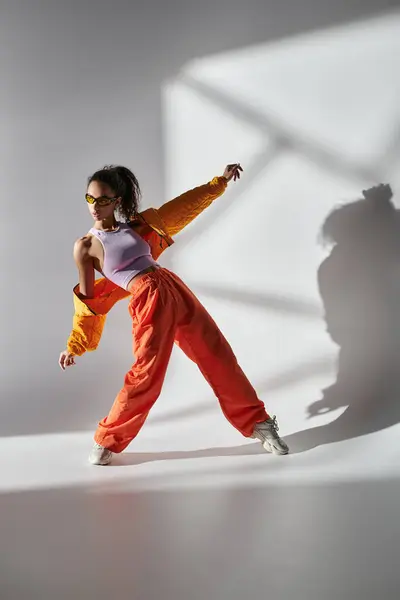 Молодая женщина в жёлтой куртке и оранжевых штанах позирует в студии на сером фоне.. — стоковое фото