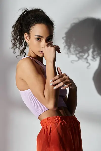 Giovane donna con i capelli ricci in studio. Canotta viola, pantaloncini arancioni. In mostra le ultime tendenze della moda Gen z. — Foto stock