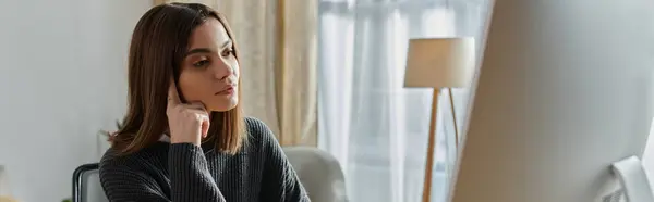 A young woman in a grey sweater sits thoughtfully in a home office, contemplating her next creative project. — Stock Photo