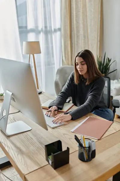 A young woman sits at a desk, typing on a computer keyboard, while working from home. — Stock Photo
