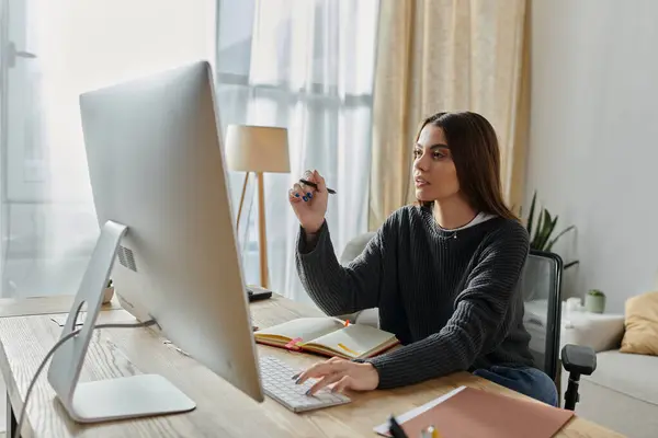 Uma jovem se senta em sua mesa, trabalhando em seu computador, focada em sua tarefa. — Stock Photo