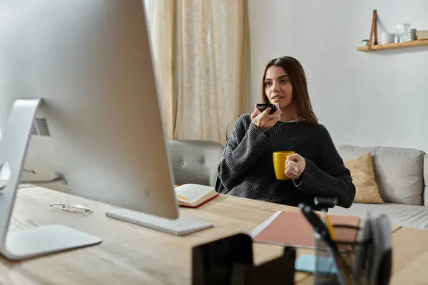 Una giovane donna si siede alla scrivania, registrando contenuti mentre si gode una tazza di caffè. — Foto stock