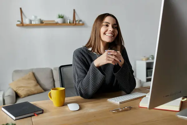 A young woman smiles brightly as she works on her computer in her home office. — Stock Photo