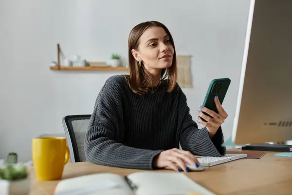 Una giovane donna con un maglione grigio lavora su un computer nel suo ufficio. — Foto stock