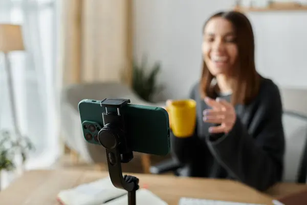 A young woman records a video from her home office, smiling and holding a mug. — Stock Photo