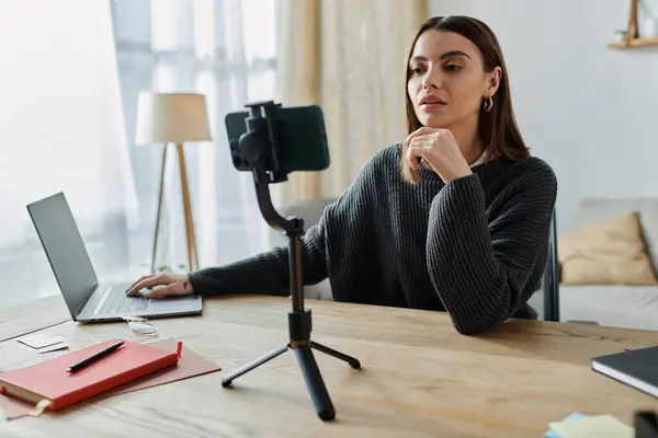 A young woman in a grey sweater sits at her desk, recording a video for her online audience. — Stock Photo