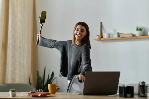 A young woman in a gray sweater films herself with a selfie stick at home. — Stock Photo