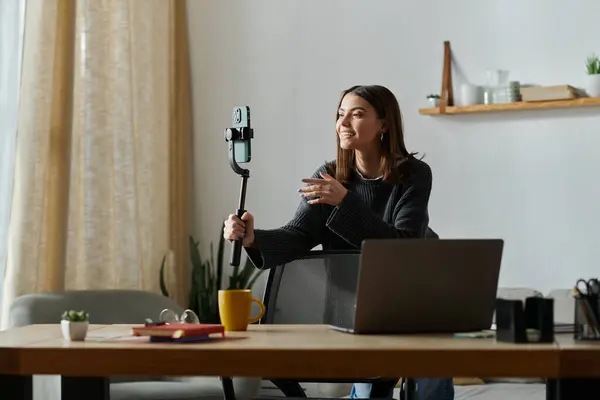 A young woman in a grey sweater sits at her desk, filming content for her online audience. — Stock Photo
