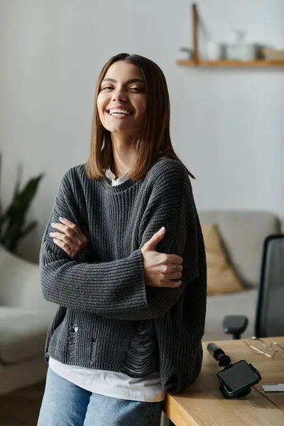 Una joven con un suéter gris sonríe con confianza mientras trabaja desde casa. - foto de stock