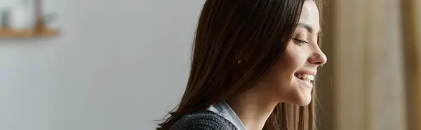 A young woman in a grey sweater smiles while working remotely from home. — Stock Photo