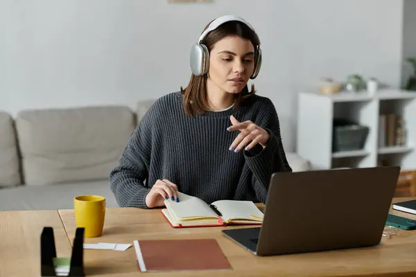 Una joven trabaja de forma remota desde casa, usando auriculares y un ordenador portátil para crear contenido y gestionar campañas de marketing digital. - foto de stock