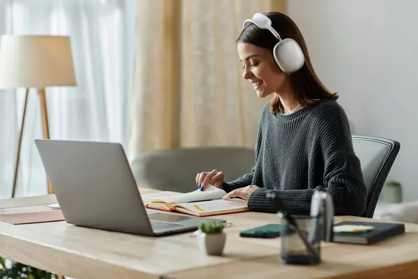 Uma mulher em fones de ouvido trabalha feliz em uma mesa em um escritório em casa, focada e confiante. — Fotografia de Stock