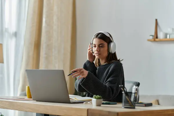 A young woman sits at a desk, wearing headphones, and working on a laptop computer. She is creating content for her business. — Stock Photo