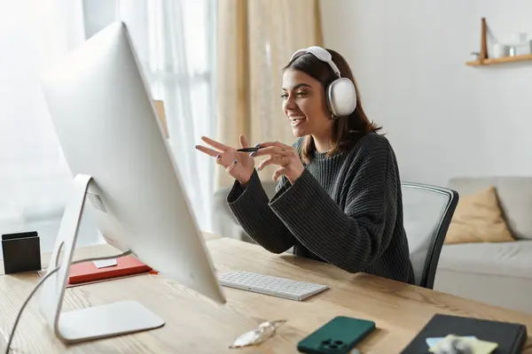 A smiling young woman wearing headphones sits at a desk, using a computer. — Stock Photo