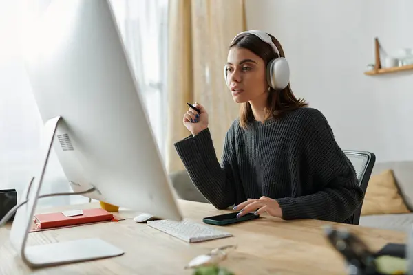 Una joven trabaja desde casa, enfocada en la pantalla de su computadora, con auriculares puestos, creando contenido atractivo. — Stock Photo