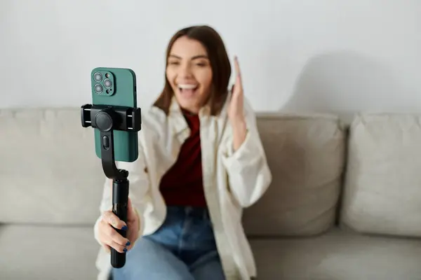 Una joven sonriente filma un vlog mientras está sentada en un sofá, usando un estabilizador para teléfonos inteligentes. — Stock Photo