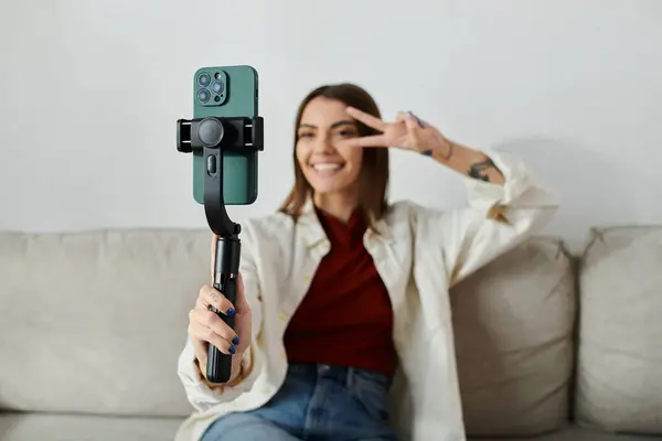 A young woman casually dressed films content for her vlog using a smartphone stabilizer, sitting on a sofa. — Stock Photo