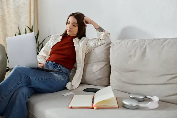 A young woman in casual clothes sits comfortably on a couch while working on her laptop. — Stock Photo
