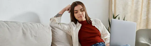 Una joven, vestida casualmente, trabaja en su portátil mientras se relaja en un sofá. - foto de stock