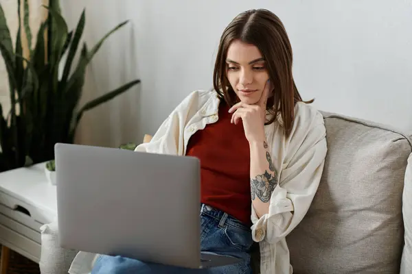 A young woman in casual attire sits on a couch, using a laptop to manage her social media accounts. — Stock Photo