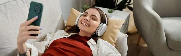 A young woman wearing headphones smiles while working on her phone, likely engaging in social media management. — Stock Photo