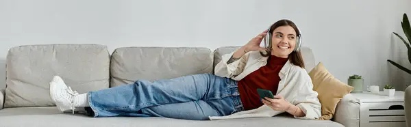 A young woman in casual attire relaxes on a couch, listening to music and working remotely. — Stock Photo