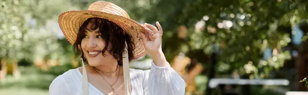 Una joven con sombrero de paja y blusa blanca sonríe mientras disfruta de un día de verano en un jardín. - foto de stock