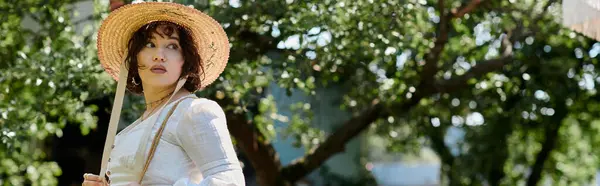 A young woman in a white blouse and straw hat stands in a summer garden, surrounded by lush greenery. — Stock Photo