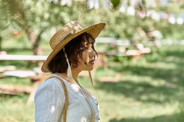 A young woman in a straw hat and white blouse strolls through a sun-drenched summer garden. — Stock Photo