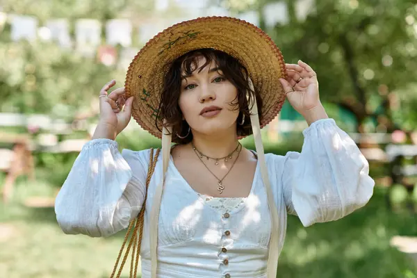Uma jovem mulher, vestida com uma blusa branca e um chapéu de palha, desfruta de um dia ensolarado de verão em um jardim exuberante.. — Fotografia de Stock
