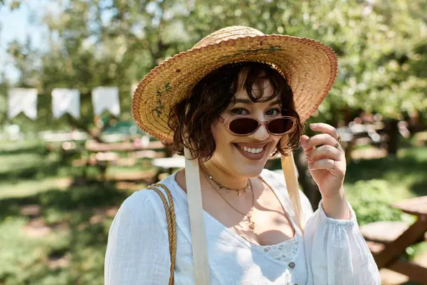 Eine junge Frau mit Strohhut und weißer Bluse lächelt, als sie in einem üppigen Garten steht. — Stockfoto