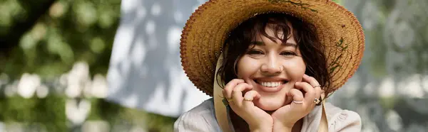 A young woman in a straw hat smiles while sitting in a summer garden. — Stock Photo