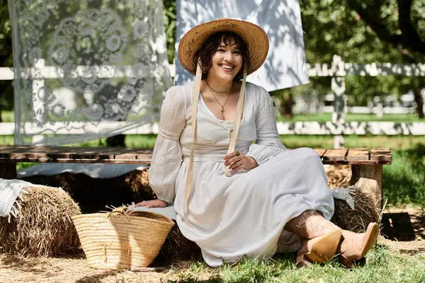 Eine Frau in weißem Kleid und Strohhut lächelt strahlend in sommerlicher Gartenkulisse. — Stockfoto