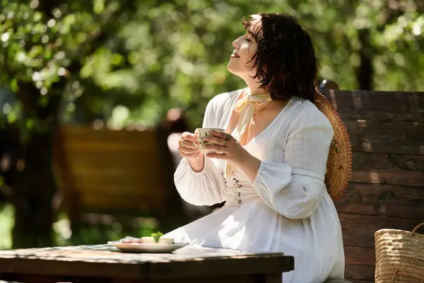 A young woman in a white dress enjoys a leisurely brunch in a summer garden, savoring the moment with a smile. — Stock Photo