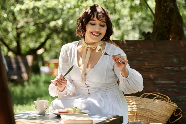 Uma jovem mulher em um vestido branco desfruta de um brunch de lazer em um jardim de verão ensolarado. — Fotografia de Stock