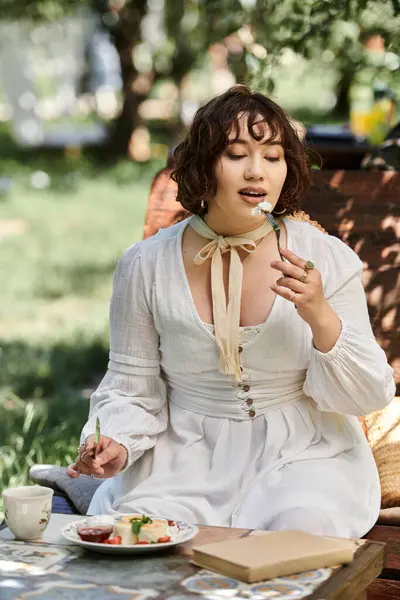 A young woman in a white dress enjoys a leisurely brunch in a summer garden, surrounded by greenery. — Stock Photo