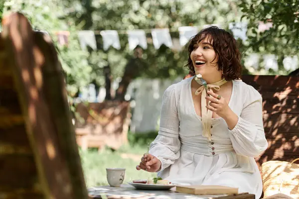 Una donna vestita di bianco si gode un brunch estivo all'aperto, sorridendo brillantemente mentre assapora una delizia dolce.. — Foto stock