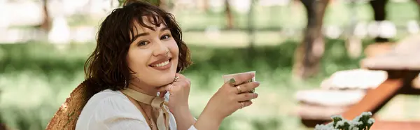 A young woman in a white dress smiles while enjoying brunch in a summer garden setting. — Stock Photo