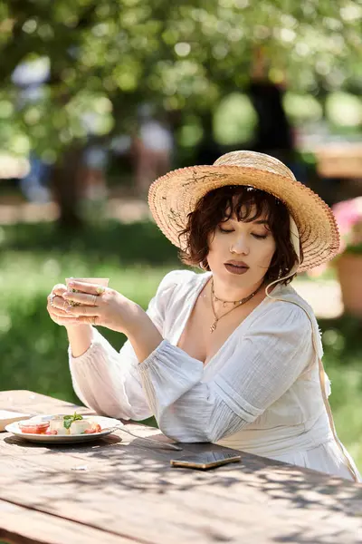 A young woman in a white dress enjoys a relaxing brunch in a summer garden, enjoying the sunshine and fresh air. — Stock Photo