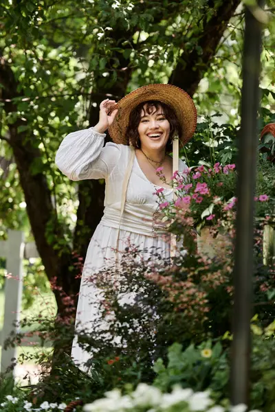 A young woman in a white dress and straw hat smiles brightly in a lush summer garden, surrounded by vibrant greenery. — Stock Photo