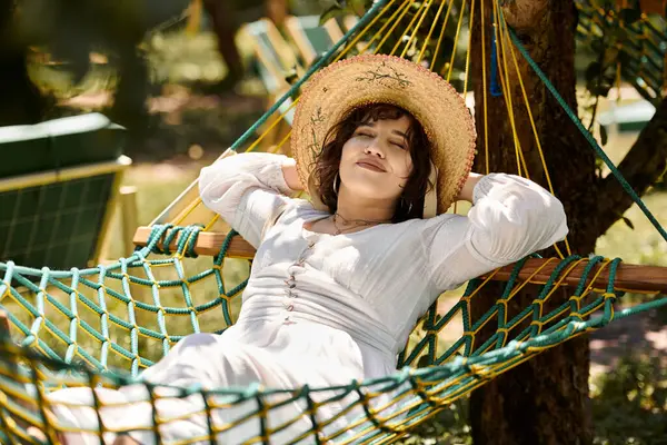 Eine junge Frau in weißem Kleid und Strohhut entspannt sich an einem sonnigen Sommertag in einer Hängematte. — Stockfoto