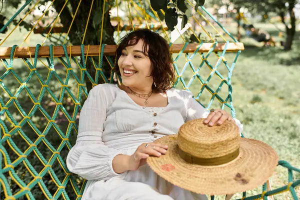 A young woman in a white dress and straw hat relaxes in a hammock on a sunny summer day. — Stock Photo