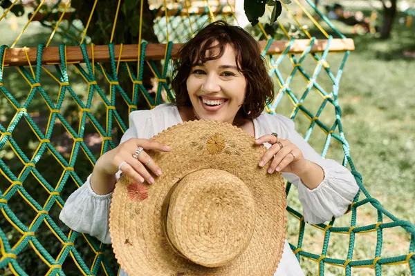 A young woman in a white dress and straw hat relaxes in a hammock on a summer day. — Stock Photo