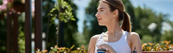 Una giovane donna in abbigliamento sportivo prende una pausa dal suo allenamento, godendo la vista da una panchina del parco. — Foto stock