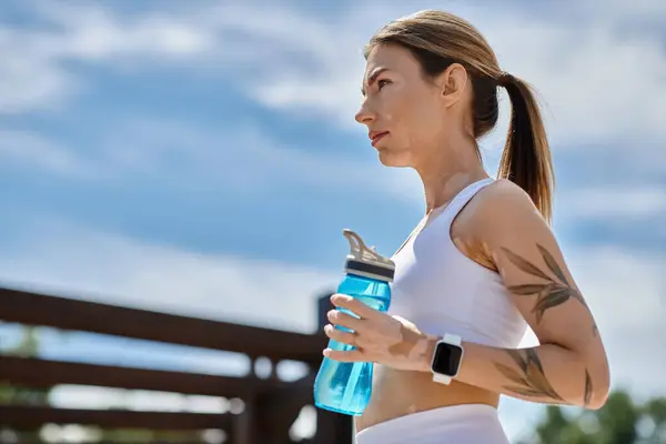 A young sportswoman with vitiligo, wearing active wear, takes a break from her workout in a park, holding a water bottle. — Stock Photo