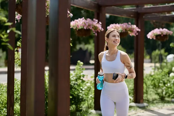 A young woman with vitiligo runs through a park, holding a water bottle and a phone. — Stock Photo