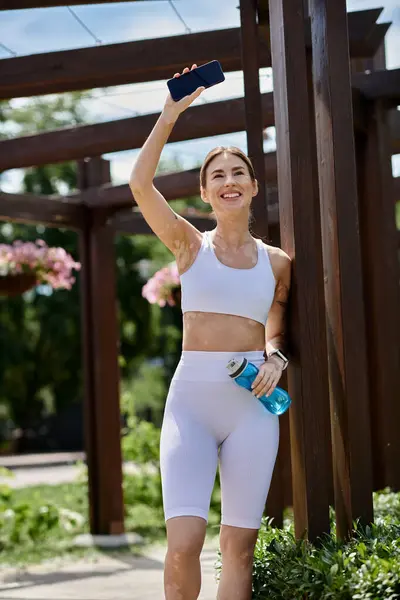 Una giovane donna in abito sportivo bianco sorride e saluta dopo un allenamento in un parco. — Foto stock